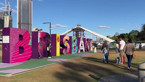 Punto-De-Referencia-Turístico-Icónico,-Letra-De-Bloque-Gigante-De-Colores-De-La-Ciudad-De-Brisbane-Con-La-Construcción-Del-Puente-Del-Río-Cruzado-En-El-Fondo-En-Un-Día-Soleado,-Queensland-El-Estado-Del-Sol,-Australia