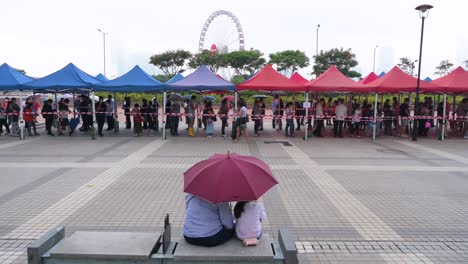 A-couple-sits-on-a-bench-in-front-of-a-queue-of-residents-to-receive-PCR-tests-for-coronavirus-from-a-Community-Testing-Centre-truck-to-tackle-the-spread-of-the-virus-and-a-pandemic-wave