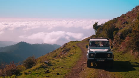 Kamerafahrt-Eines-Weißen-Jeeps,-Der-Auf-Einer-Gefährlichen-Landstraße-Auf-Einem-Hohen-Berg-über-Wolken-Fährt