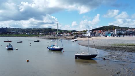 Aerial-view-moored-boats-on-Welsh-low-tide-seaside-breakwater-harbour-coastline-right-orbiting-slowly