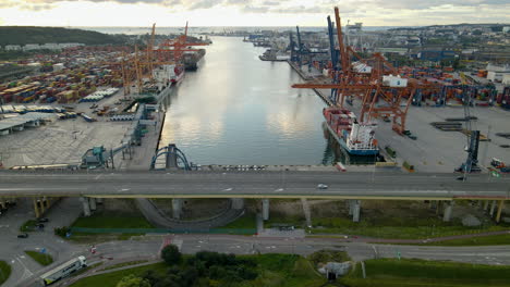 Panorámica-Aérea-A-Lo-Largo-Del-Puente-Y-El-Puerto-De-Gdynia-Con-Grúas-Gigantes-Cargando-Contenedores-De-Carga-En-Cargueros-Al-Atardecer