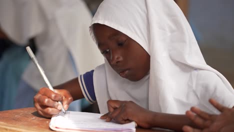 Niña-Islámica-Estudiando-En-La-Escuela-Con-Un-Pañuelo-Blanco-En-La-Cabeza-Y-Escribiendo-En-Su-Cuaderno