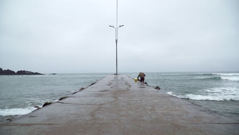 Un-Pescador-En-Un-Muelle-Con-Olas-Oceánicas-En-San-Bartolo,-Lima,-Perú