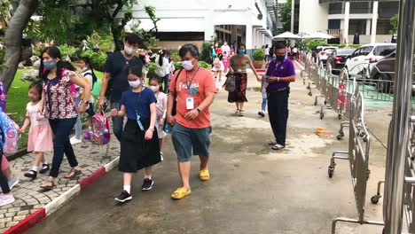 Padres-Asiáticos-Recogiendo-A-Pequeños-Estudiantes-Después-De-La-Escuela-Por-La-Noche,-Todas-Las-Personas-Con-Máscaras-Médicas