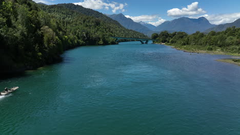 Aerial-Following-Speed-Boat-Along-Puelo-River-Approaching-Low-Bridge-In-Chile,-Lake-District