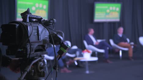 An-impressive-close-view-behind-the-camera:-an-operator-is-shooting-a-discussion-between-men-in-suits-seated-in-comfortable-chairs