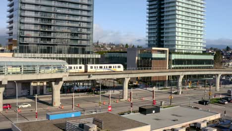 Tren-Que-Sale-De-La-Estación-Del-Centro-De-La-Ciudad-De-Brentwood,-Estación-De-Metro-Elevada-Sobre-La-Autopista-Lougheed-En-Canadá