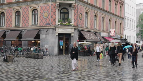 People-In-Umbrellas-Passing-By-A-Bakery-Store-In-Copenhagen,-Denmark-On-A-Rainy-Day