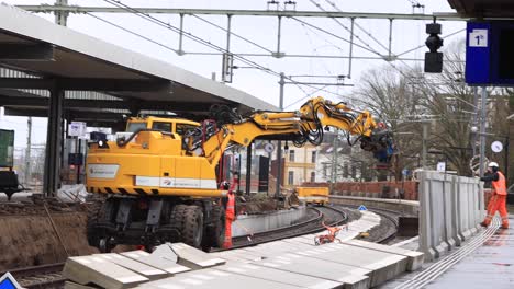 Arbeiter-Bei-Wartungsarbeiten-Und-Bauarbeiten-An-Bahngleisen-In-Zutphen-Mit-Schweren-Maschinen,-Die-Große-Blöcke-An-Ihre-Stelle-Setzen