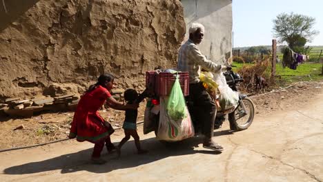 Child-running-behind-old-motorcycle-driven-by-elderly-man-with-white-hair-and-beard,-Noondpura-village,-Rajasthan