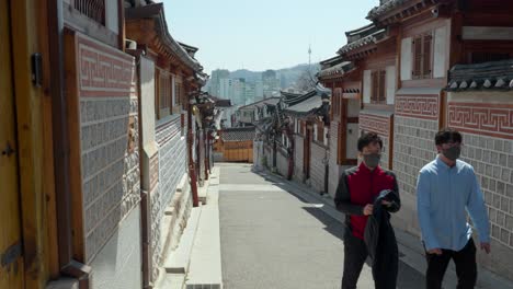 Dos-Viajeros-Con-Mascarillas-Respiratorias-Viajan-En-El-Pueblo-De-Bukchon-Hanok-En-Seúl,-Corea-Del-Sur