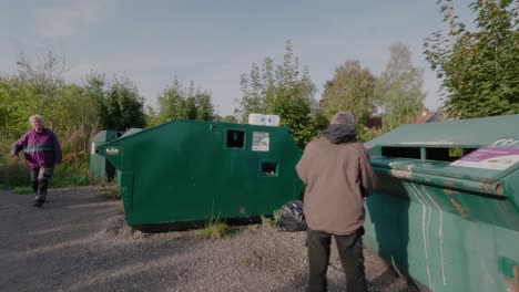 Una-Pareja-De-Ancianos-Arroja-Basura-En-La-Estación-De-Reciclaje,-Seguimiento-Amplio-A-La-Derecha