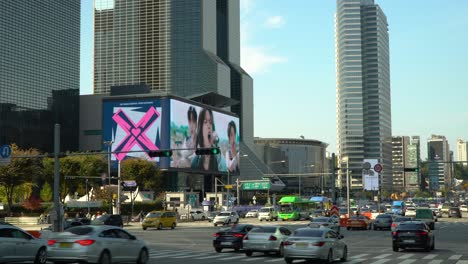 Seoul-Cars-traffic-near-COEX-on-Yeongdong-daero-road-passing-Samseong-station-intersection,-Trade-Tower,-Parnas-skyscraper,-Asem-Building,-STtown-Coex-Outdoor-Digital-Billboard-over-blue-sky