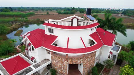 Nuevo-Techo-De-Ladrillo-Rojo-En-Una-Casa-Blanca-De-Tres-Pisos-Para-Unas-Relajantes-Vacaciones-En-Vadorara,-India,-Rodeada-Por-Un-Gran-Lago-Con-Bosque-Tropical-Y-Un-Cielo-Azul-Claro