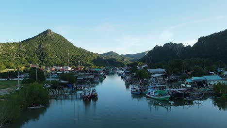 A-revers-aerial-footage-revealing-mountains-and-fantastic-blue-sky,-the-fishing-village-with-boats-moored