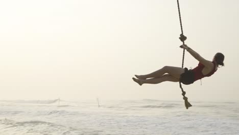 Mujer-Se-Balancea-Desde-Una-Palmera-Sobre-El-Océano-Durante-El-Amanecer-En-La-Playa-Paraíso