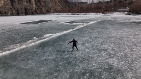 Luftaufnahme-über-Der-Silhouette-Eines-Erwachsenen-Mannes,-Der-Auf-Dem-Zugefrorenen-Khalti-See-Im-Ghizer-Tal-Schlittschuhlaufen-Lernt