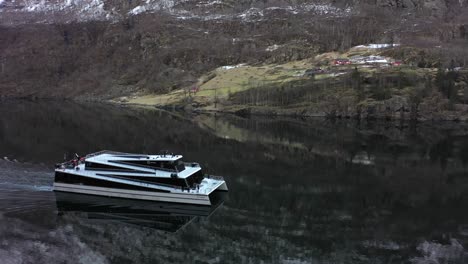 Tourists-enjoying-cruise-through-Unesco-listed-Naeroyfjorden-onboard-electric-and-modern-Passenger-catamaran-Vision-of-the-fjords---Aerial-following-ships-side-while-approaching-Gudvangen