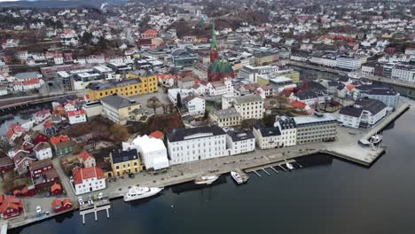 Acercándose-A-La-Histórica-Iglesia-De-La-Trinidad-En-Arendal-Noruega---Antena-Desde-La-Costa-Hacia-Tyvholmen-Y-El-Centro-De-La-Ciudad