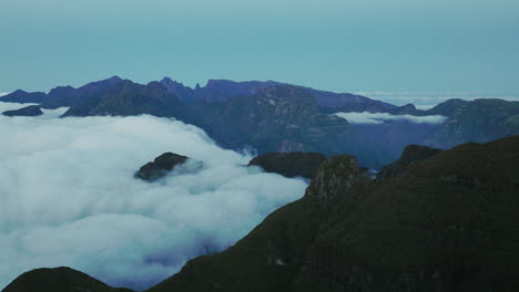 Drone-view-of-clouds-flowing-down-mountain-plateau-to-lower-valley