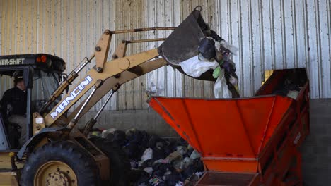 Der-Eimer-Eines-Bulldozers-Kippt-Den-Abfall-In-Den-Trichter-Eines-Förderbandes-In-Einer-Abfallverarbeitungsanlage