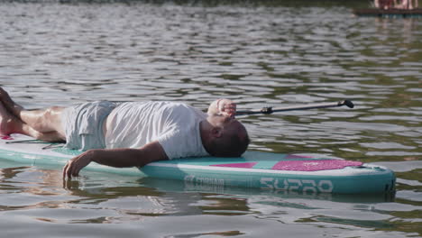 Älterer-Mann-Liegt-Auf-Dem-Paddleboard-Und-Ruht-Sich-Nach-Dem-Paddeln-Auf-Dem-Teich-Oder-See-Aus,-Nahaufnahme