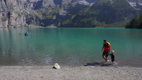 Vater-Und-Sohn-Halten-Sich-Beim-Spielen-An-Einem-Klaren,-Blauen-Bergsee-In-Den-Schweizer-Alpen-An-Den-Händen