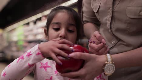 Little-girl-looking-at-a-red-pepper,-holding-her-mother's-hand