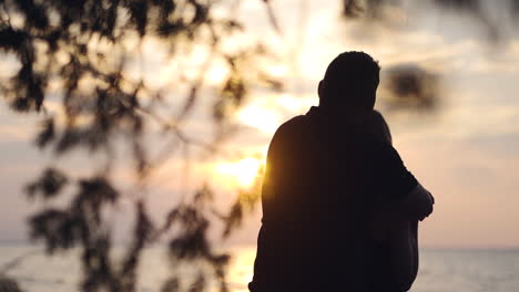 Couple-holding-each-other-and-looking-across-a-lake-during-sunset