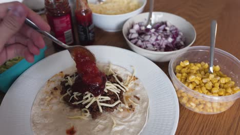 Putting-some-hot-taco-sauce-on-ground-taco-meat-laying-on-a-tortilla-bread