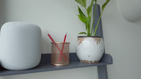 Toma-Panorámica-A-La-Derecha-De-Un-Homepod-De-Apple-En-La-Parte-Superior-De-Una-Estantería-De-Aspecto-Moderno-Junto-A-Un-Portalápices---Planta