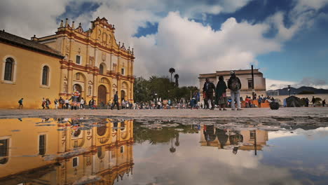 MAIN-CATHEDRAL-AND-RAIN-REFLECTION-ON-THE-FLOOR-IN-SAN-CRISTOBAL-DE-LAS-CASAS,-CHIAPAS-MEXICO-SHOT-PEOPLE-PASSING-BY