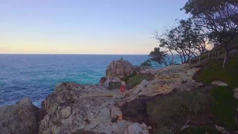 Aerial-view-of-a-man-sitting-on-a-cliff-during-sunset