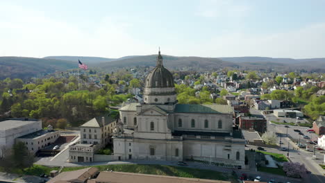 Aerial-drone-view-of-the-Cathedral-of-the-Blessed-Sacrament-in-Altoona,-Pennsylvania-with-the-American-flag-seen-behind