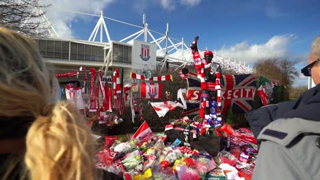 La-Gente-Presenta-Sus-Respetos-En-La-Estatua-De-Los-Bancos-De-Gordon-Junto-Al-Estadio-De-La-Ciudad-De-Stoke,-La-Gente-Firma-Camisetas,-Bufandas,-Banderas-Y-El-Libro-Del-Recuerdo