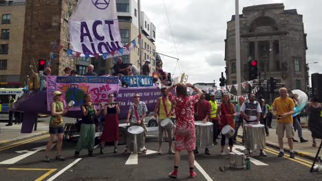 Demonstranten-Der-Extinction-Rebellion-Spielen-Musik-Vor-Einem-Lila-Boot,-Das-Eine-Der-Hauptstraßen-Im-Stadtzentrum-Von-Glasgow-Blockiert