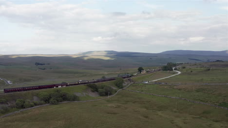 Toma-Aérea-Del-Tren-De-Vapor-Flying-Scotsman-60103-Que-Pasa-Por-La-Estación-Ribblehead-En-North-Yorkshire-Con-Una-Amplia-Cosecha