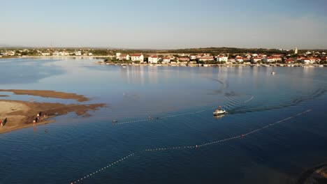 Luftpanorama-Einer-Neun-Stadt-Mit-Lagune-Und-Folgendem-Boot,-Das-Sich-Im-Sonnenuntergang-Dem-Sandstrand-Nähert