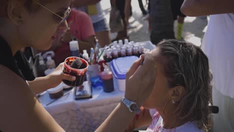 Make-up-artist-applying-products-painting-a-young-woman-in-a-wheelchair-before-Halloween-walk-of-zombies-on-the-Day-of-the-Dead-in-Copacabana