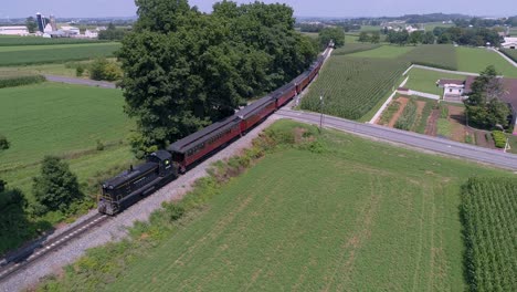 Una-Vista-Aérea-De-Una-Locomotora-Diésel-Tirando-De-Coches-De-Pasajeros-Antiguos-A-Través-De-La-Campiña-Amish