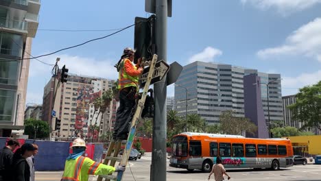 Un-Reparador-Profesional-En-Una-Escalera-Portátil-Usando-Herramientas-Para-Arreglar-Un-Semáforo-Roto-En-La-Concurrida-Intersección-De-Pershing-Square-En-El-Centro-De-Los-ángeles