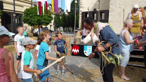 Slow-motion-of-peasant-children-kicking-and-hitting-the-court-jester-at-the-main-square,-Medieval-reenactment,-Preludij-festival-in-Slovenj-Gradec-slovenia