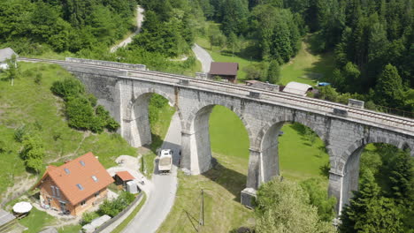 Verfolgen-Sie-Aus-Der-Vogelperspektive-Einen-LKW,-Der-Auf-Der-Landstraße-Fährt-Und-Unter-Dem-Eisenbahnviadukt-In-Slowenien-Vorbeifährt