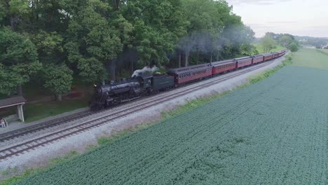 Vista-Aérea-De-Un-Tren-De-Pasajeros-De-Vapor-Que-Se-Aproxima-En-La-Campiña-Amish-En-Un-Día-De-Verano