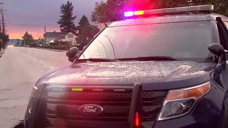 Coche-De-Policía-Al-Atardecer-Después-De-Una-Tormenta-Con-La-Luz-Encendida