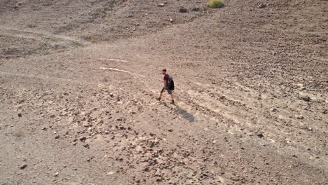 Aerial-circular-shot-from-drone-of-an-young-male-walking-in-a-rocky-desert-valleys-in-Hatta,-United-Arab-Emirates