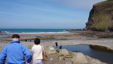 Un-Par-De-Turistas-Mayores-Se-Detienen-En-La-Playa-De-Crackington-Haven-En-Cornualles,-Reino-Unido,-Donde-Los-Caminantes,-Nadadores-Y-Bañistas-Se-Divierten