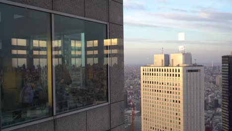 Personas-Dentro-De-La-Oficina-Mirando-La-Metrópolis-A-Través-De-La-Pared-De-Vidrio-De-Un-Edificio-Alto-En-Tokio,-Japón---Tiro-Medio