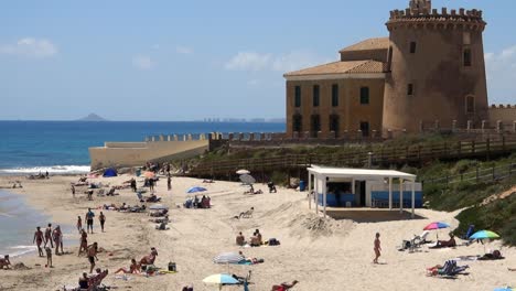 Torre-de-la-Horradada-near-Torrevieja-in-Spain,-and-people-on-beach-in-front-of-it