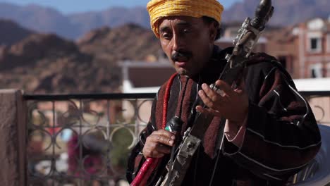 Backlit-closeup-shot-of-berber-musician-playing-bowed-instrument-rabab-and-singing-traditional-songs-in-Tafraoute,-Morocco